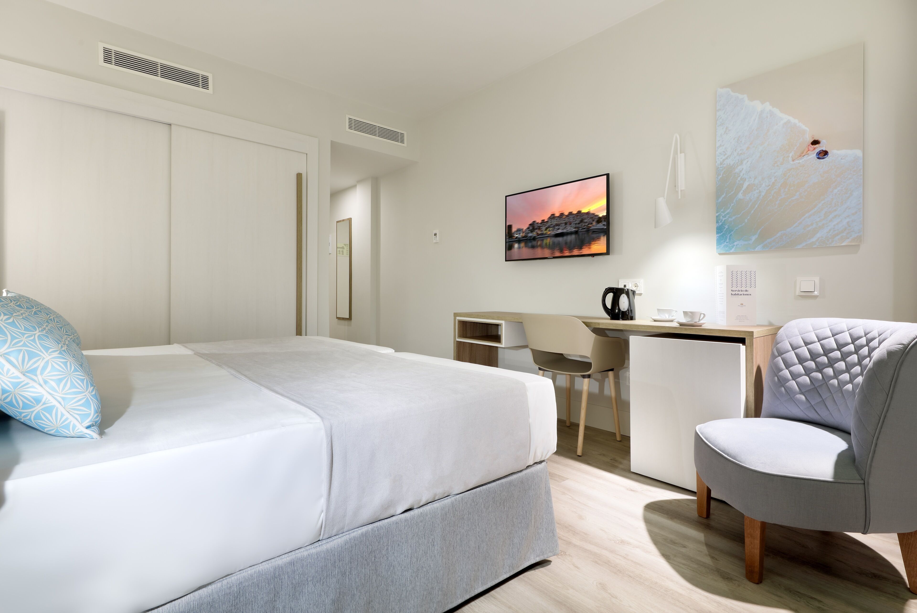 A hotel room with a bed, a desk, a chair, and a painting on the wall.