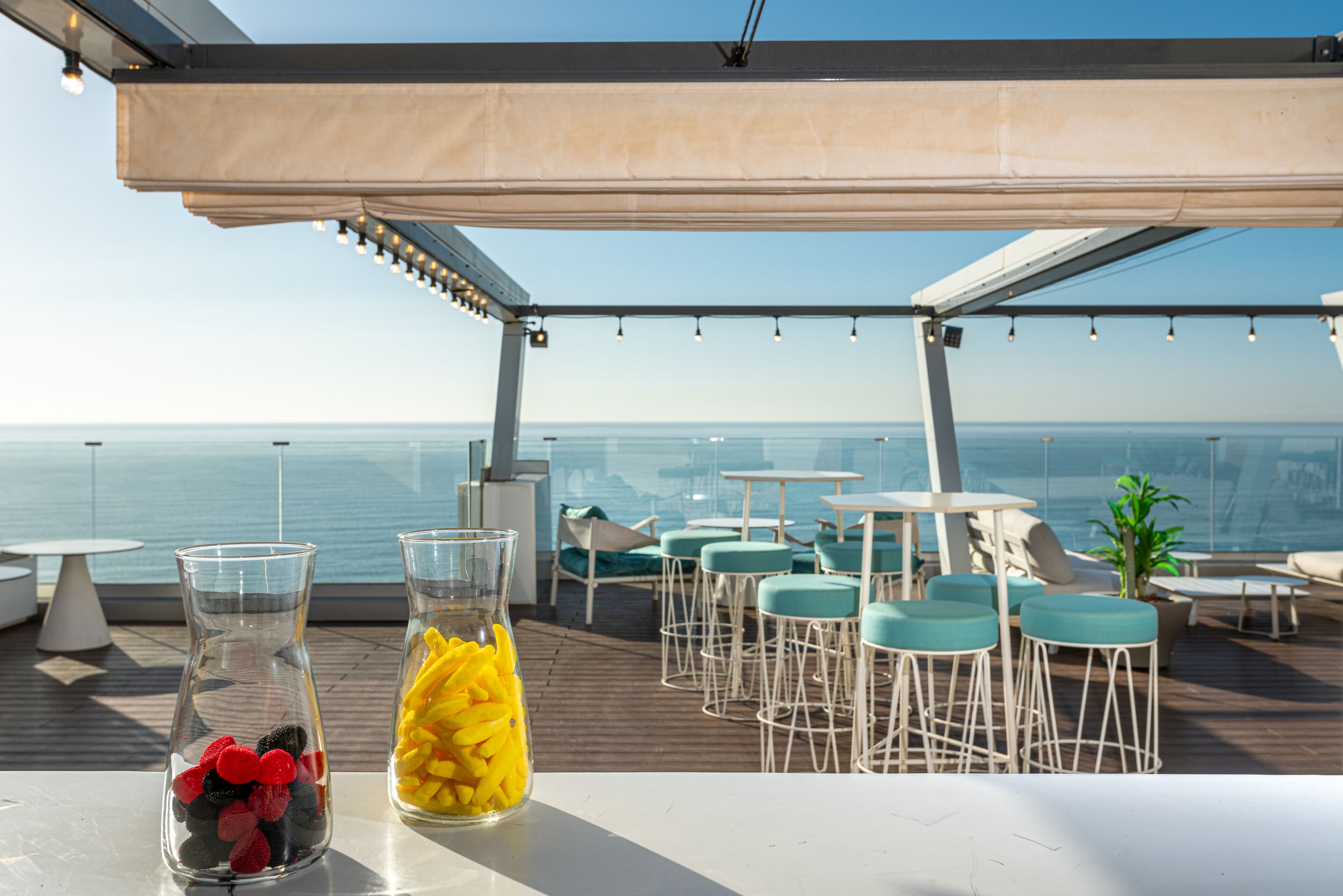 A rooftop bar with tables and chairs, overlooking the sea.