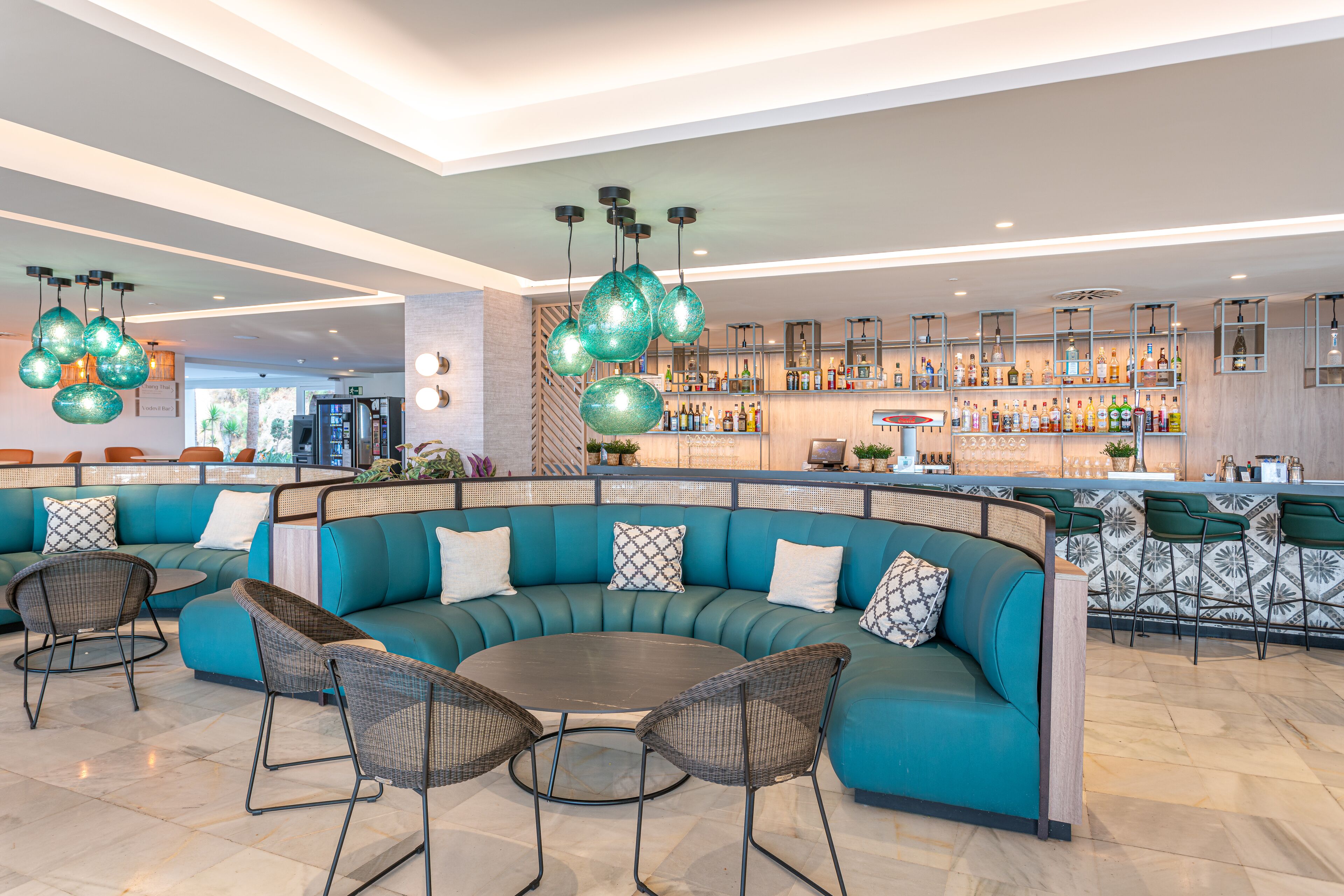 Un área de bar moderna con asientos color turquesa, una mesa redonda y globos verdes colgantes.