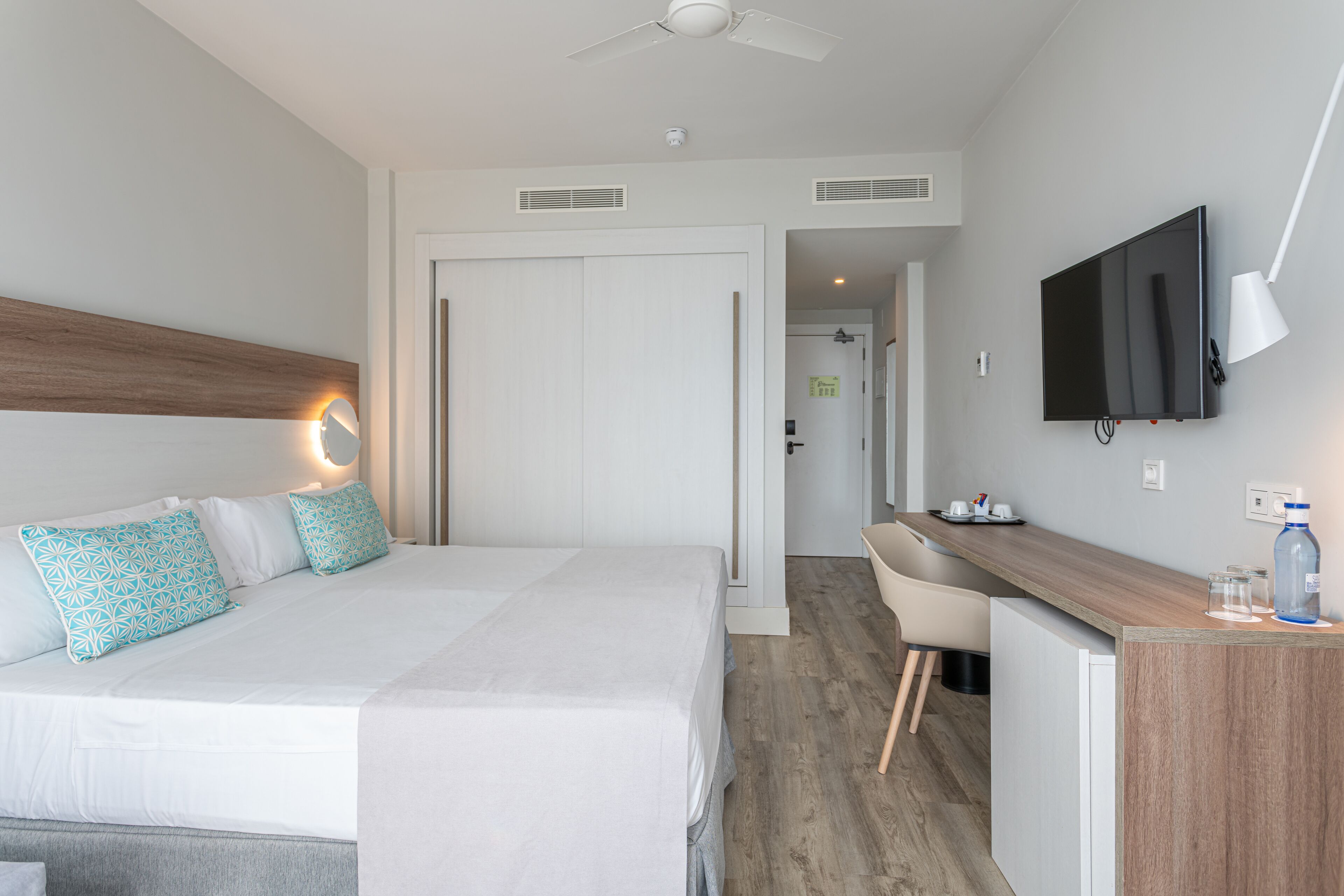 Una habitación de hotel con cama, escritorio, televisión y ventilador de techo.