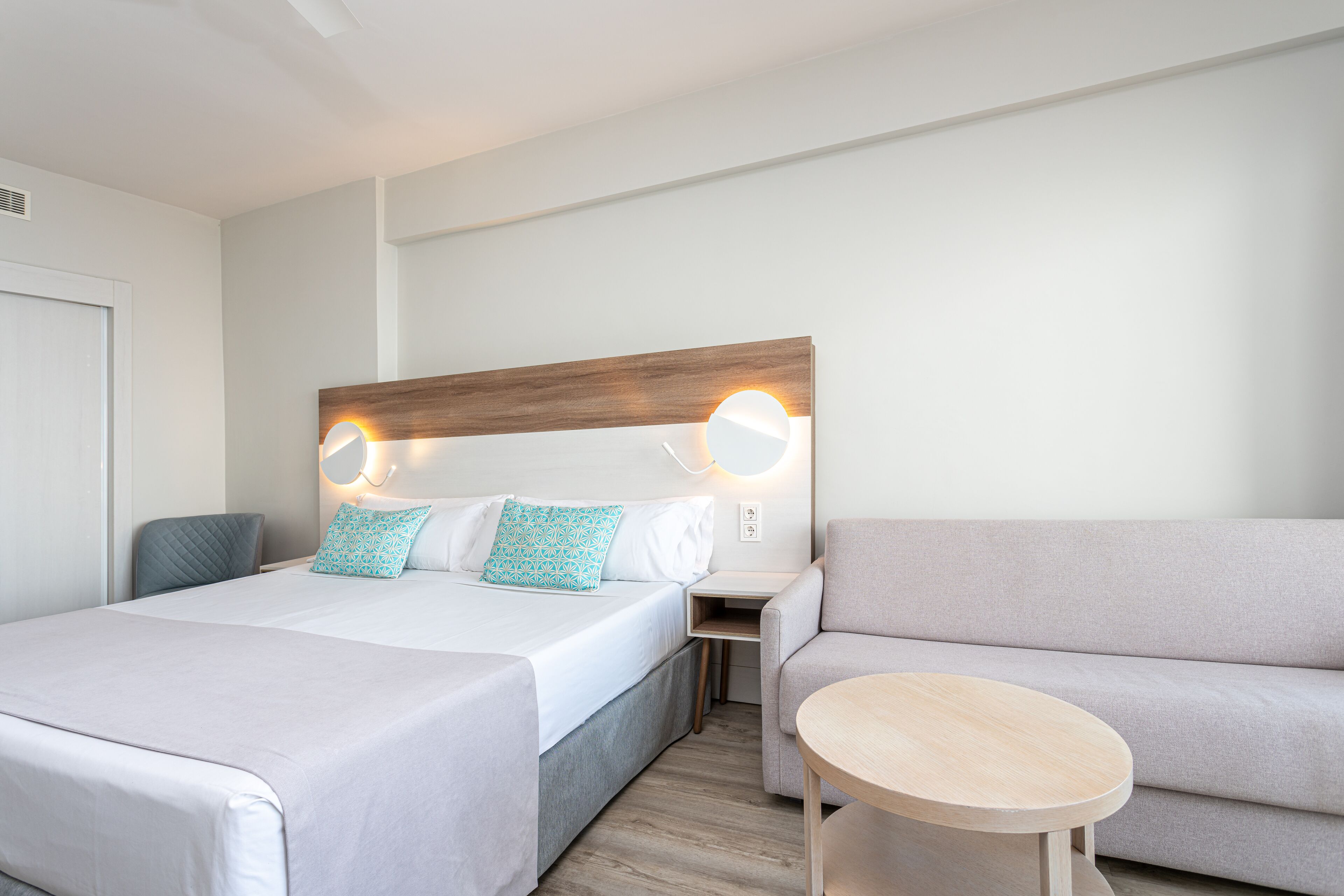Camera d'albergo con un letto grande, un divano, un tavolino e un comodino con una lampada.