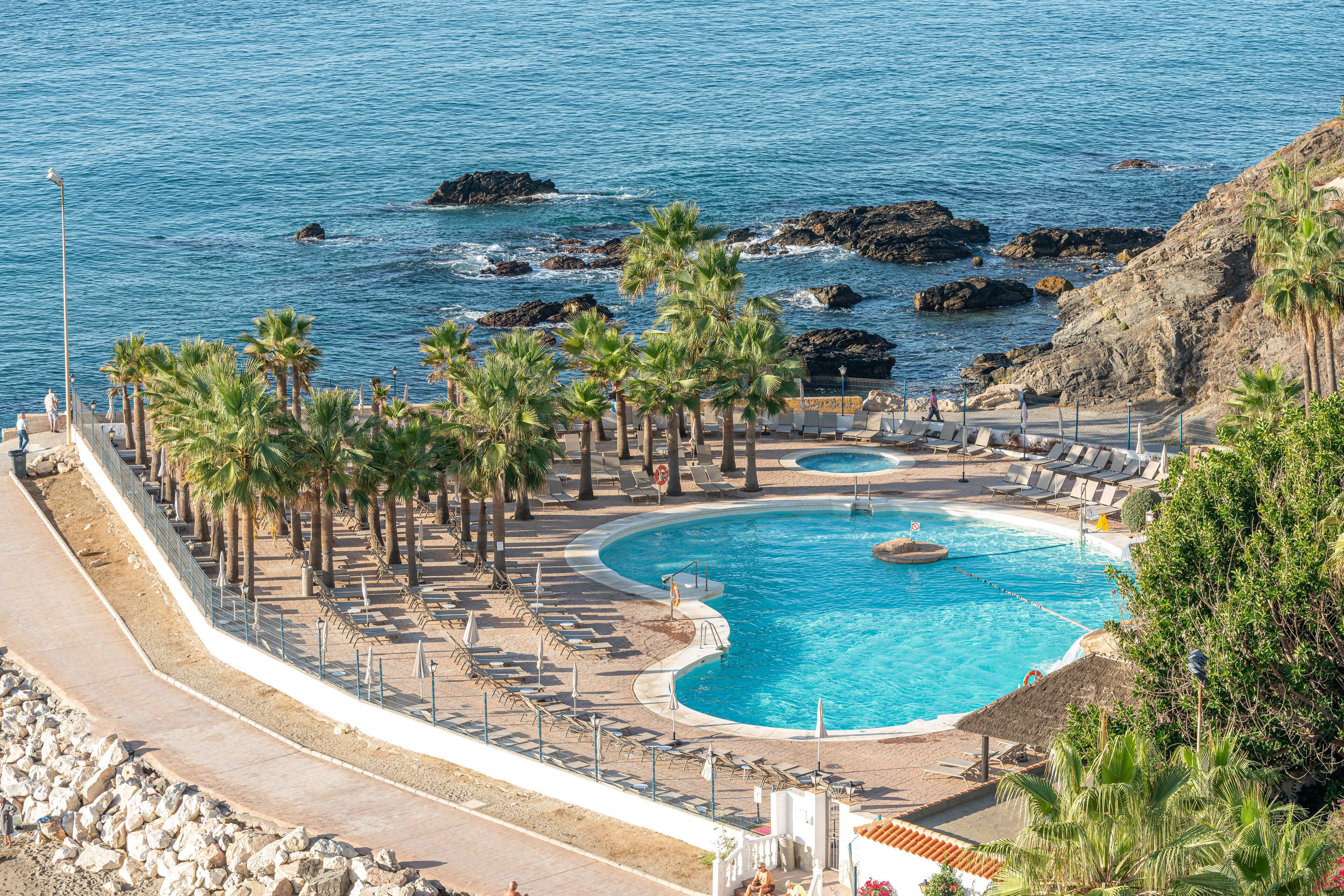 Un resort con una piscina grande, palmeras y vistas al mar.