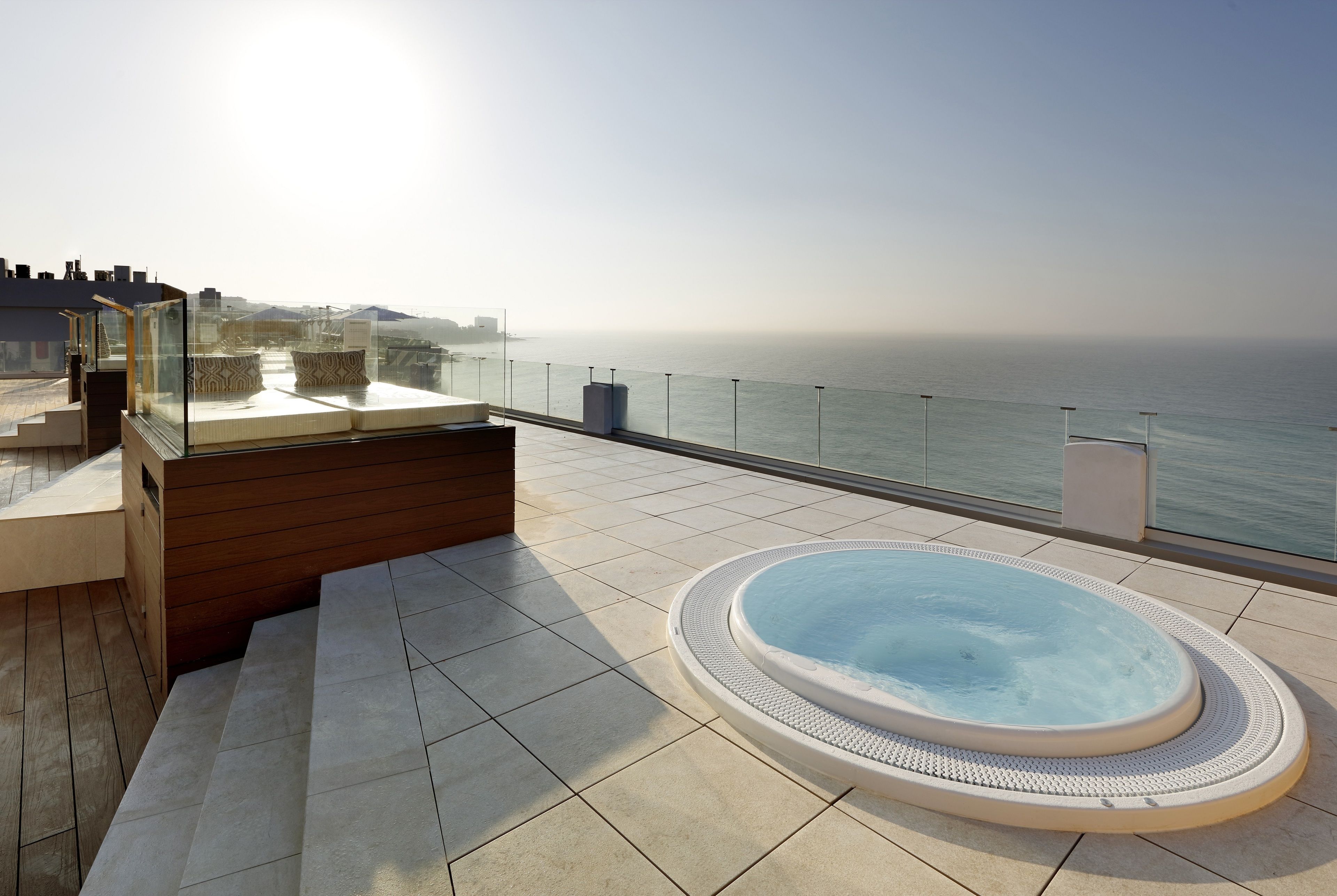 Eine Dachterrasse mit Whirlpool, einer Glasreling und Blick auf das Meer.