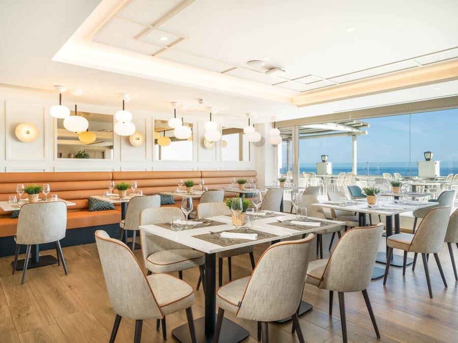 Un restaurante moderno con mesas altas y asientos cómodos, ventanas amplias que ofrecen vistas al océano y lámparas de diseño contemporáneo.