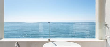 A balcony with a round table and two chairs, overlooking a calm sea.