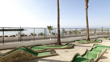 Un campo de mini golf con un sendero pavimentado, palmeras y vista al mar.
