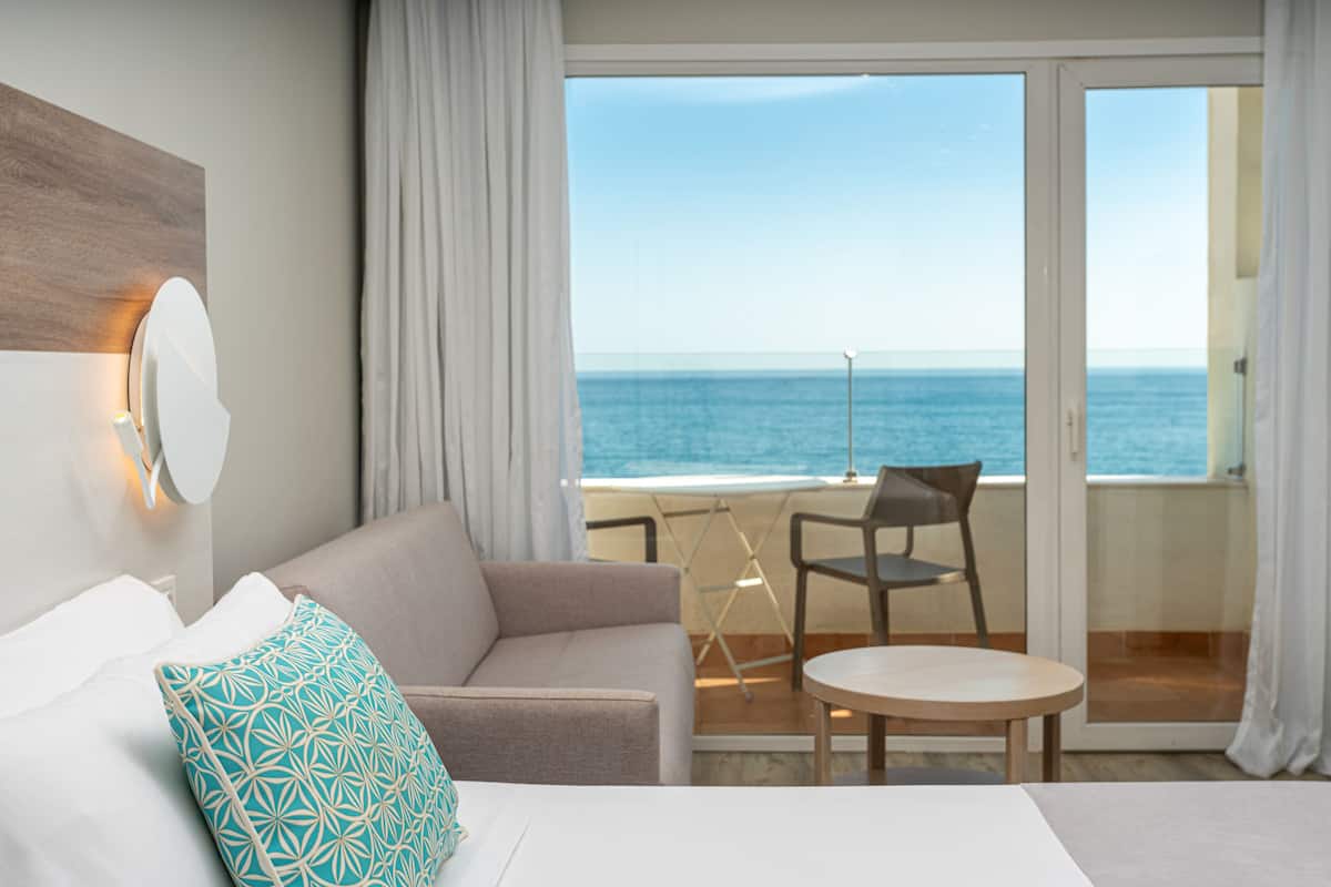 A hotel room with a balcony, a sofa, a small table, and a view of the sea.