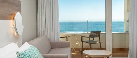 Ein Hotelzimmer mit Balkon, einer Couch, einem kleinen Tisch und Meerblick.