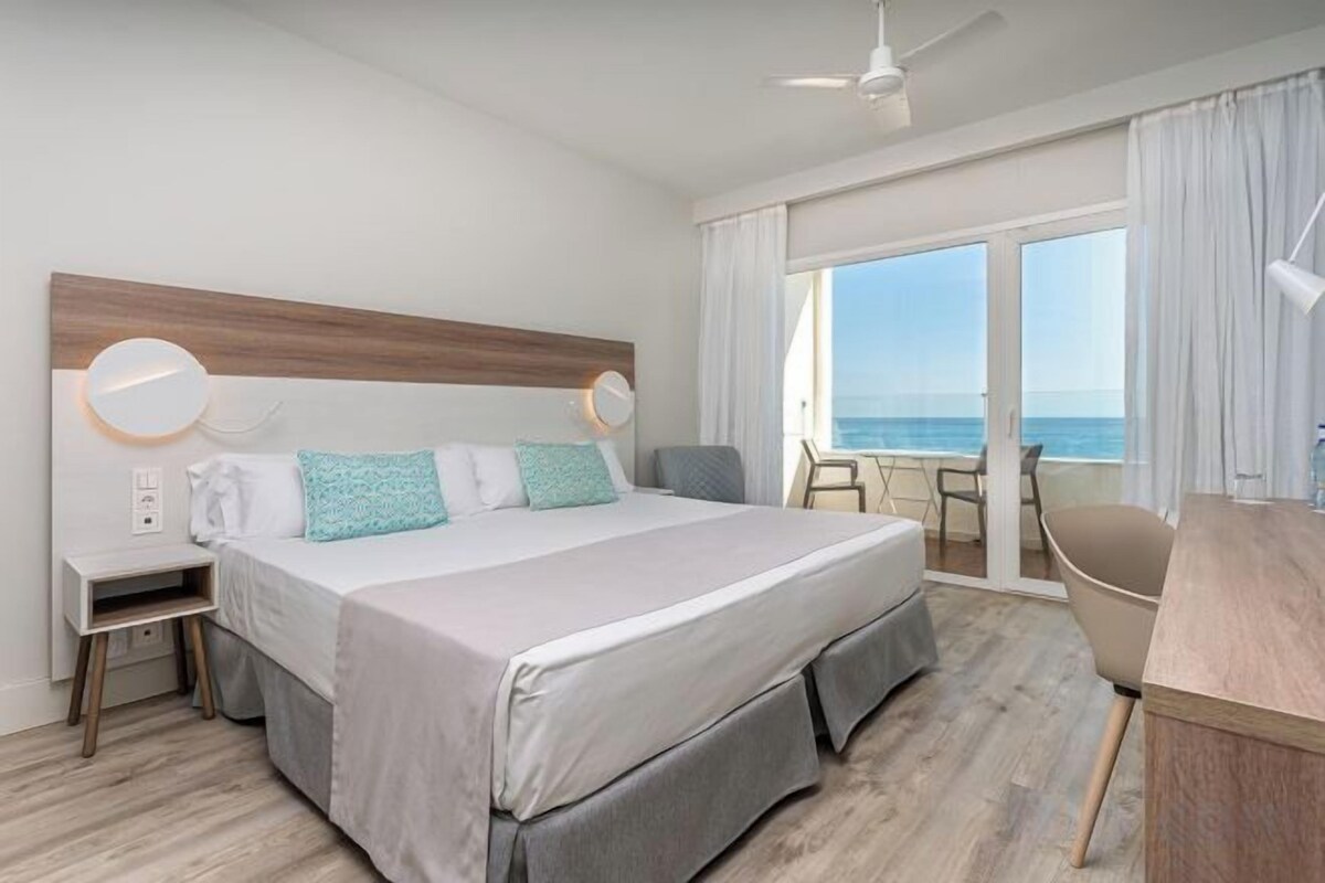 Habitación de hotel con una cama grande, un escritorio, una silla y vistas al mar.