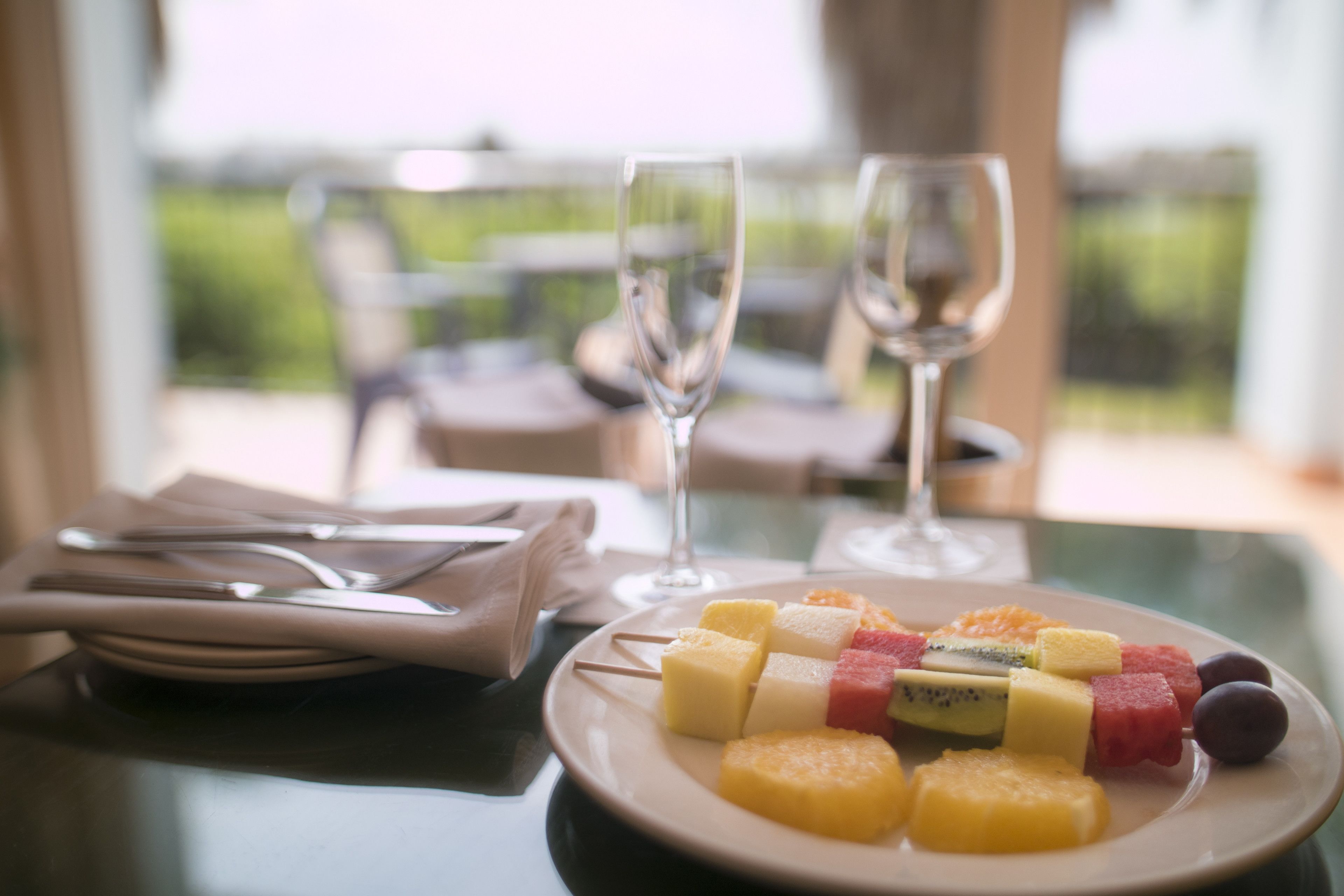 Una mesa con una bandeja de frutas, dos copas de vino y un mantel doblado con cuidado.