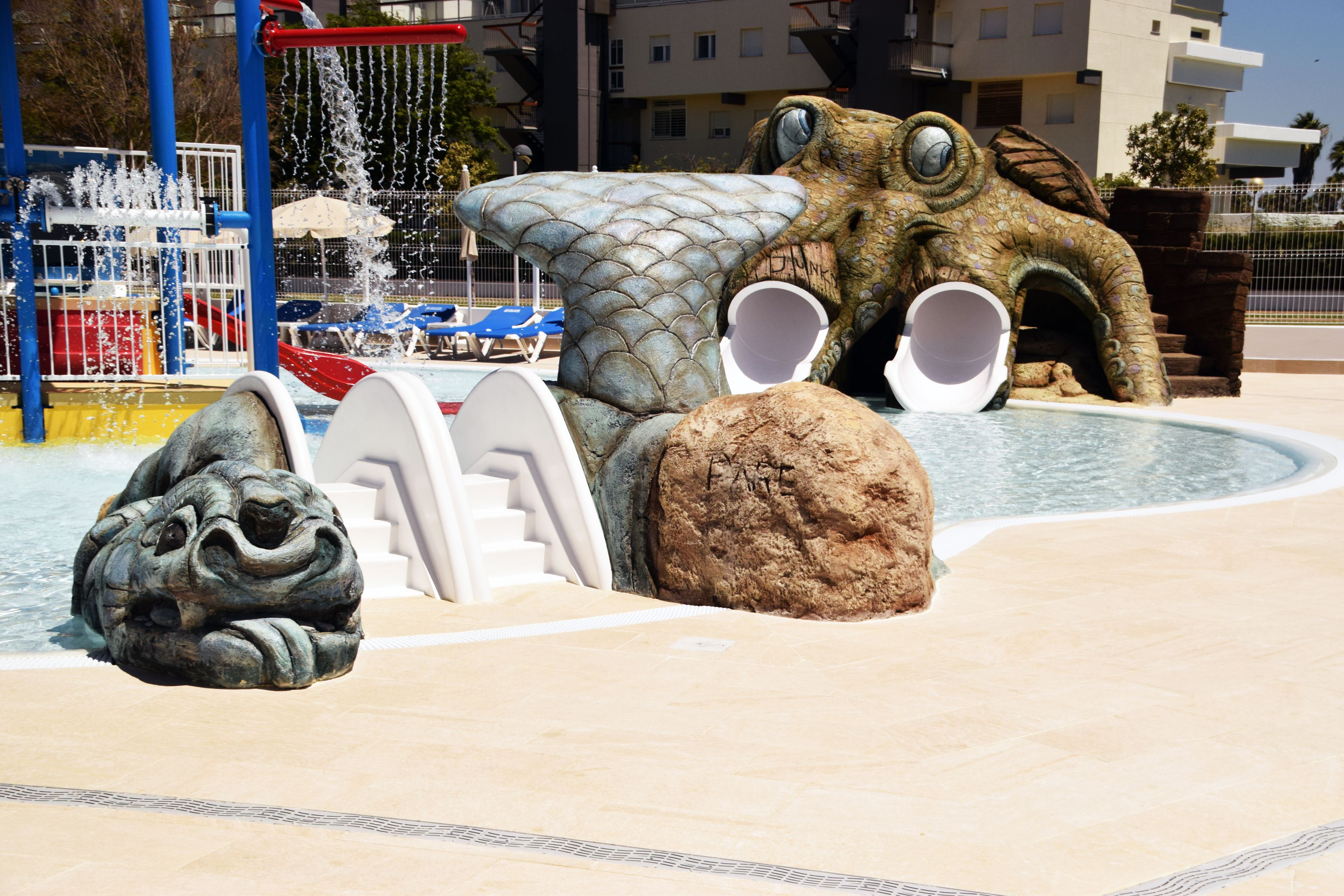 Un área de juegos acuáticos con una gran escultura de cocodrilo, un tobogán y una piscina.