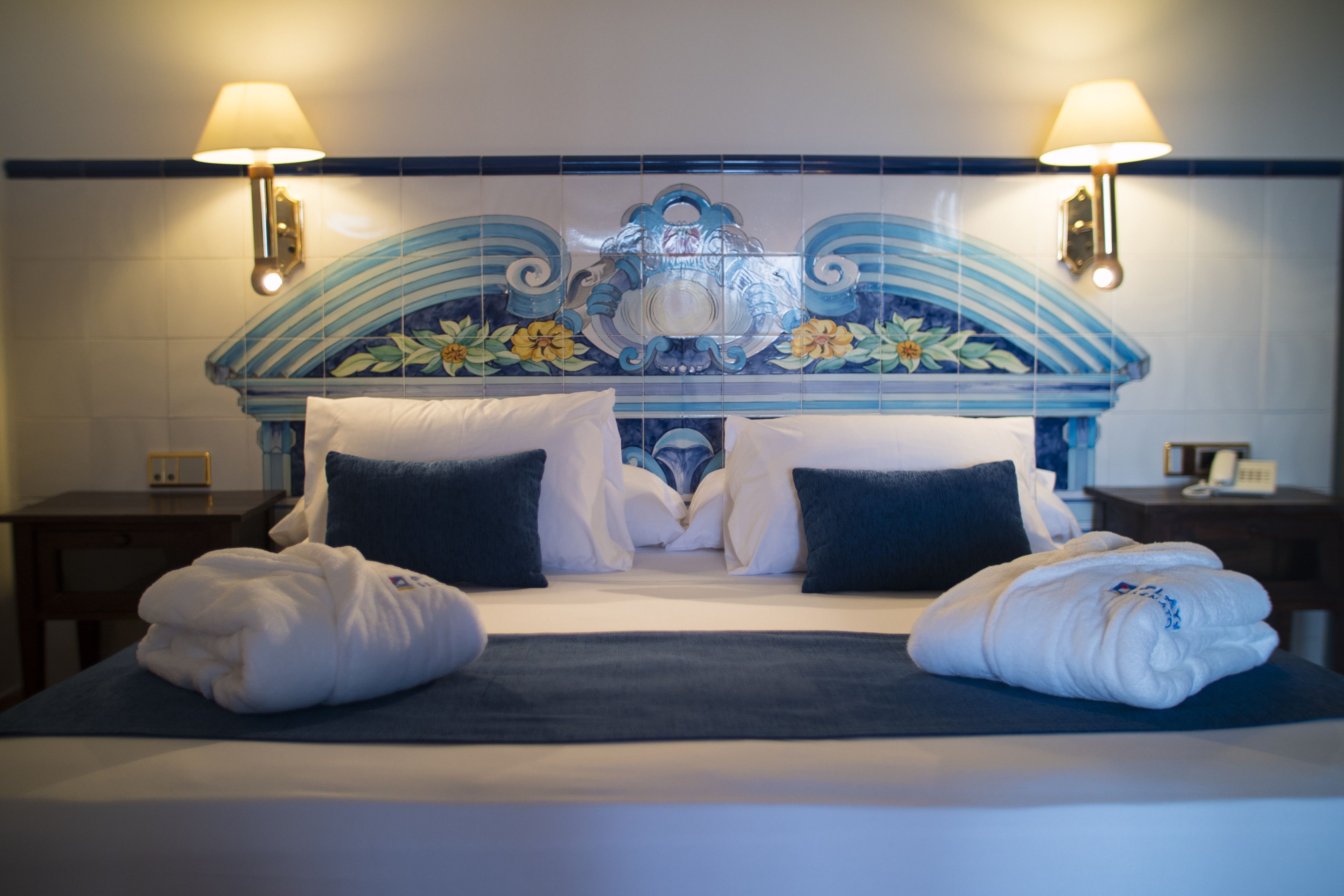 Une chambre d’hôtel avec un lit, deux lampes de chevet et une tête de lit décorative.