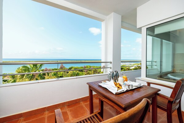 Un balcón con una mesa lista para el desayuno, con vistas a un paisaje costero.