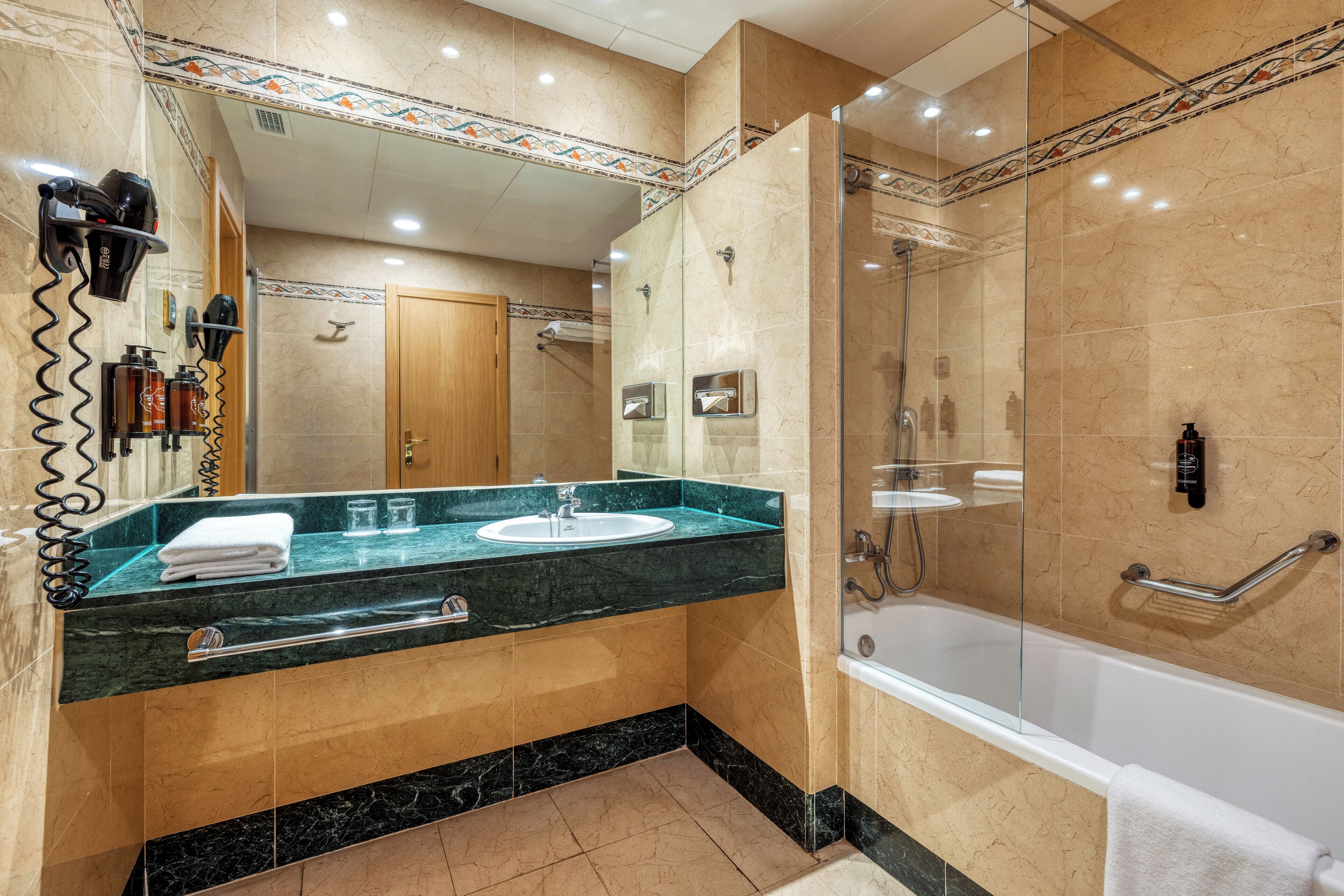A modern bathroom with a glass-enclosed shower, a sink with a marble countertop, and a wooden door in the background.