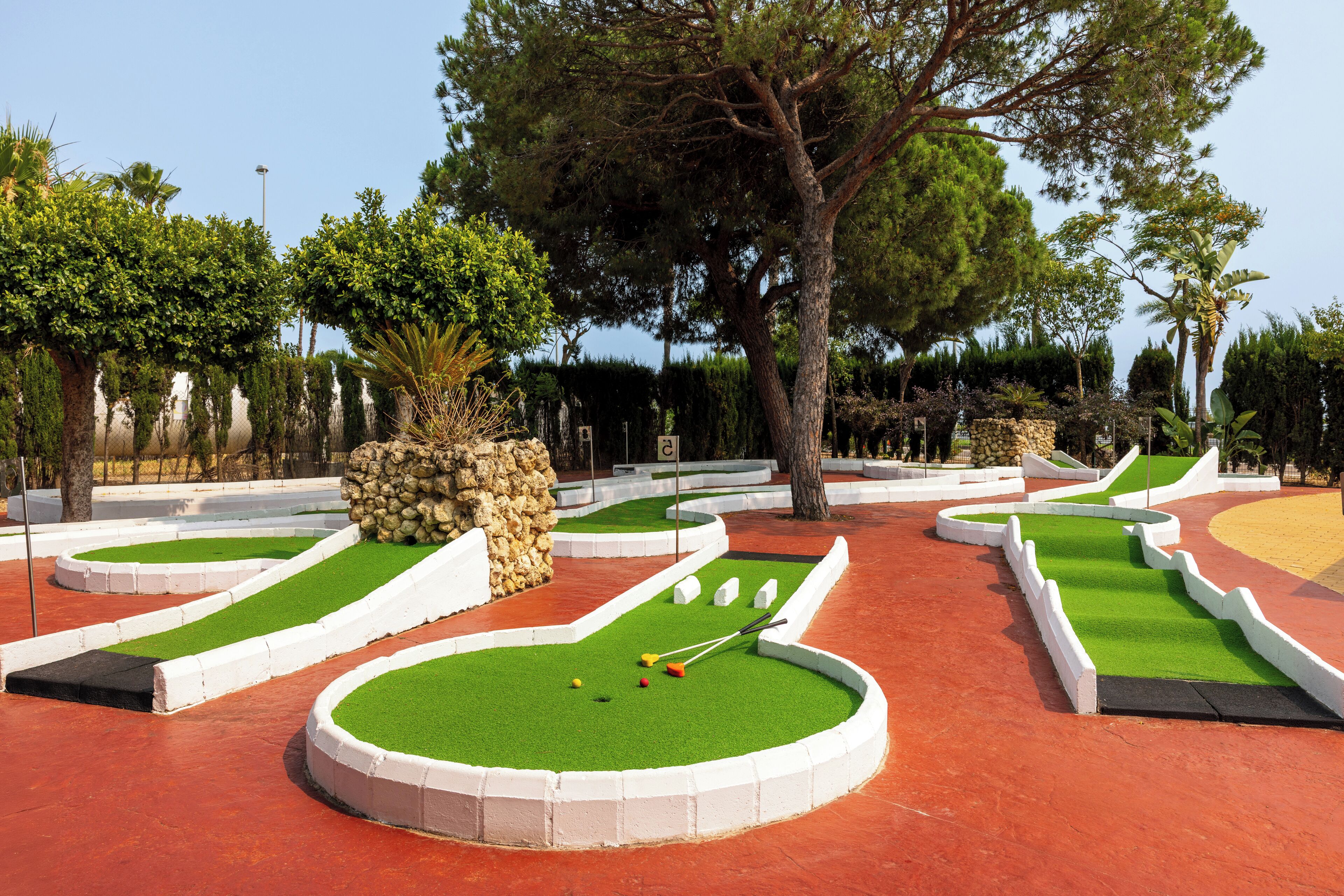 A miniature golf course with multiple holes, surrounded by trees and a stone wall.