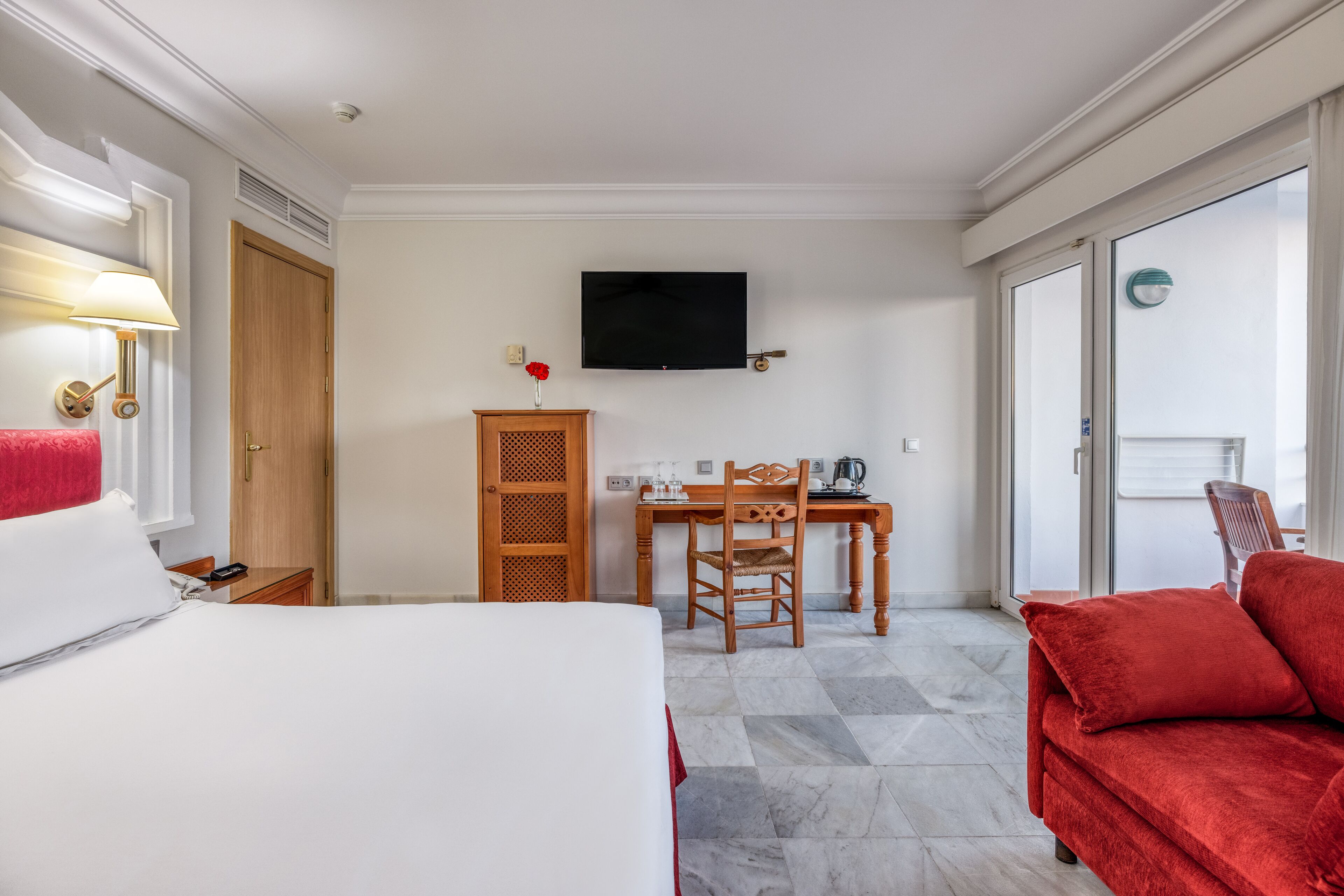 Habitació d'hotel amb un llit, una taula de treball, una cadira, un televisor i un sofà vermell.