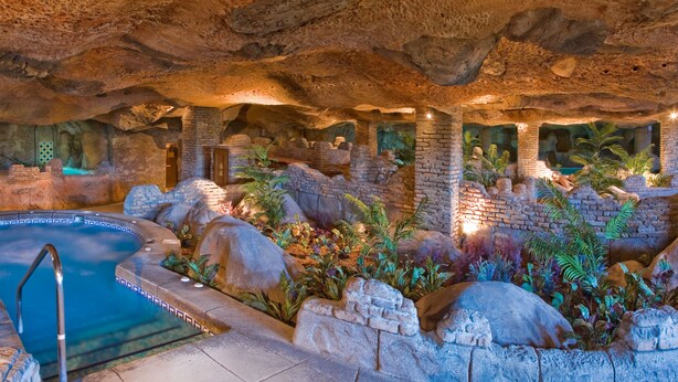 Una piscina interior con decoración de roca y plantas naturales, rodeada de muros y arcos de piedra.