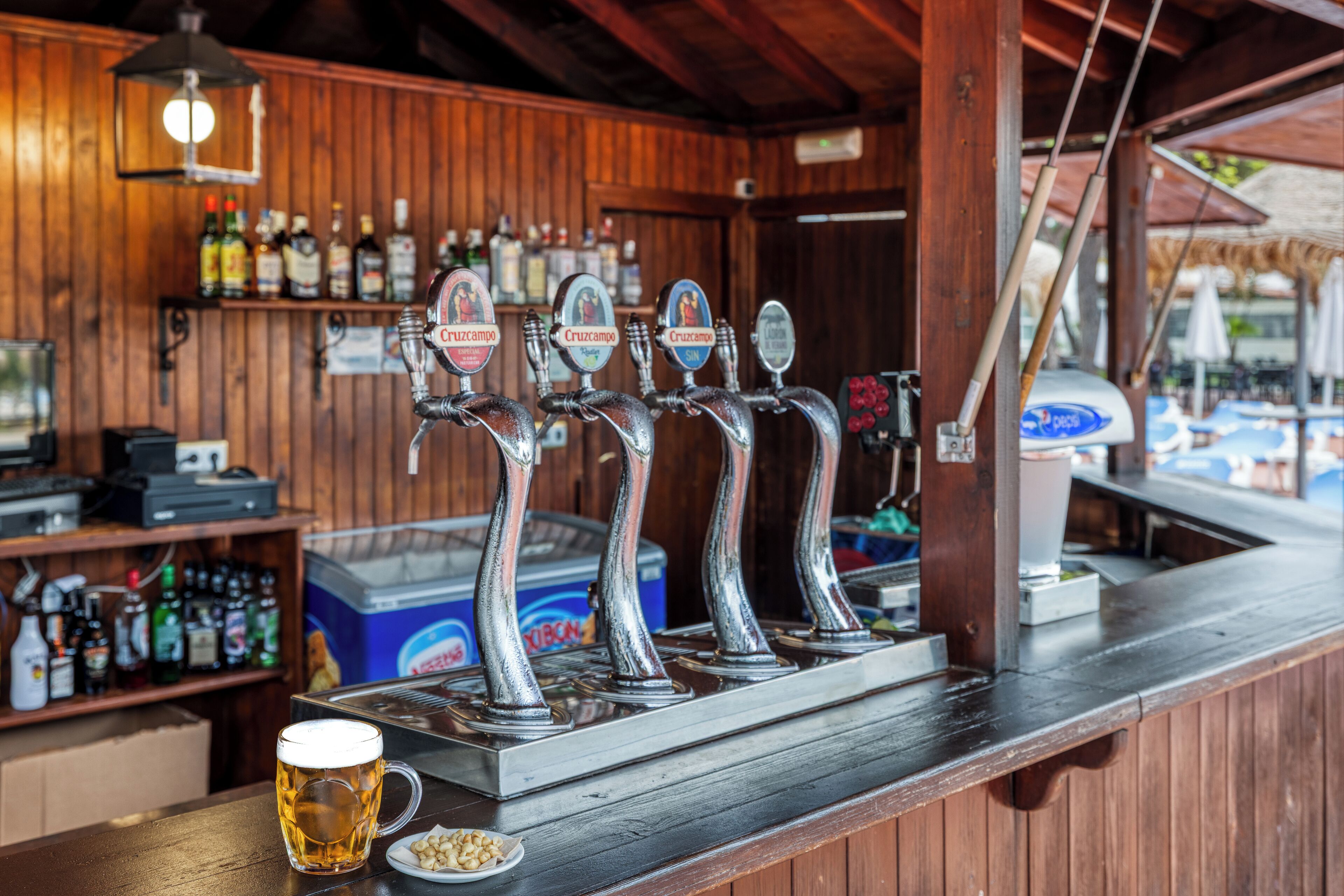 Un bar con cuatro grifos de cerveza etiquetados como 'Cruzcampo' y una jarra de cerveza sobre el mostrador.