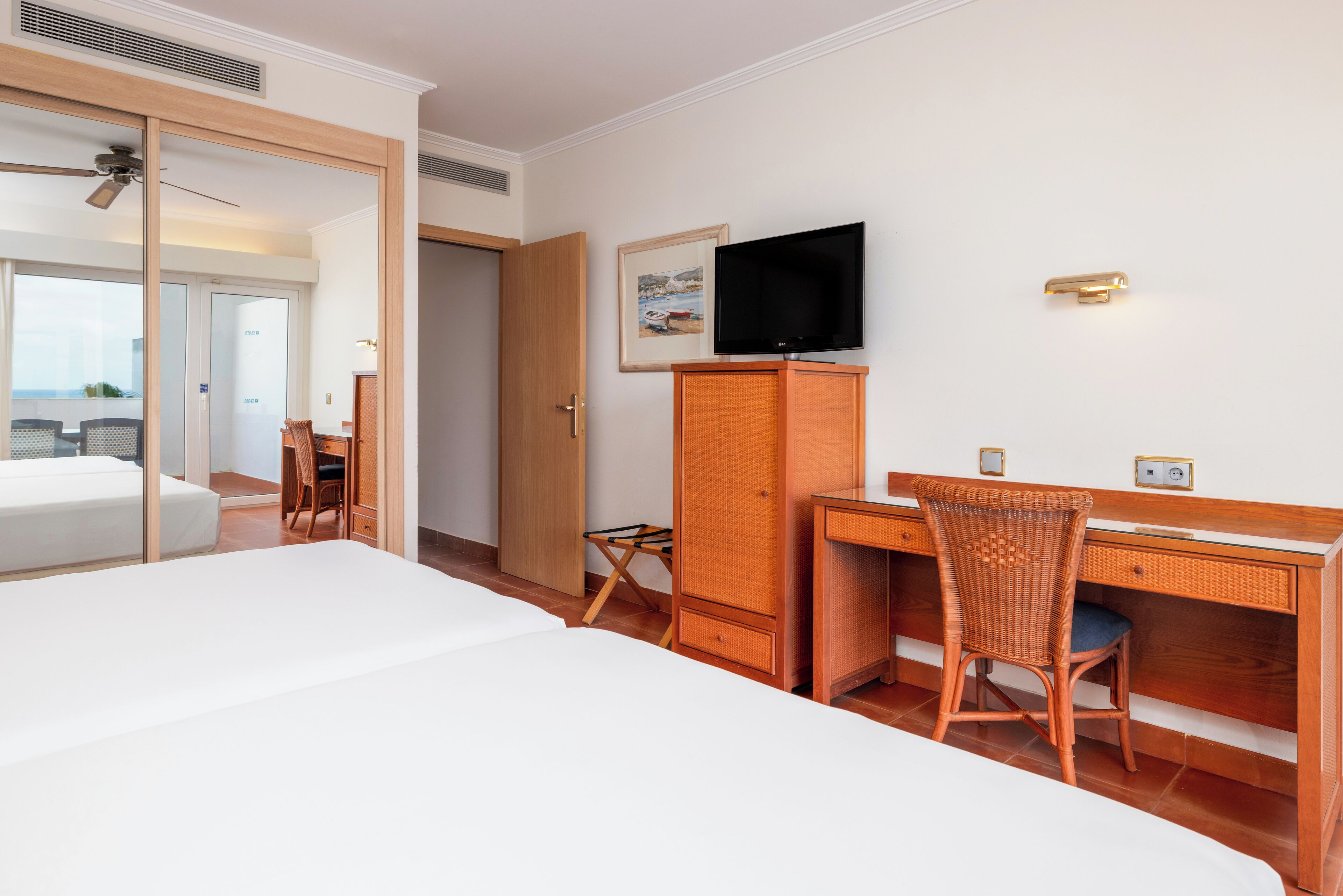 A hotel room with a bed, a desk with a chair, a television, and a wardrobe.