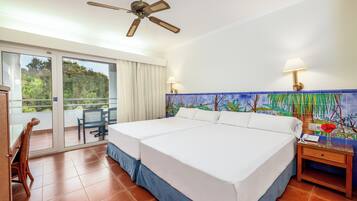 A hotel room with a large bed, a ceiling fan, a balcony with a chair, and a decorative wall mural.