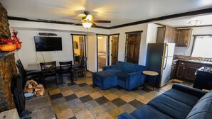 A living room with a blue sectional sofa, a dining area with a table and chairs, a kitchen with wooden cabinets, and a ceiling fan. - Timberline Lodge (Big Bear Lake)