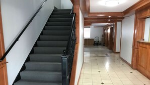 A staircase with carpeted steps and a black handrail, leading to a hallway with wooden walls and a tiled floor. - Studio 6 Suites Tupelo, MS - North (Tupelo)