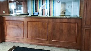 A reception desk with a laptop, a large decorative letter 'H', and a colorful striped wall in the background. - Studio 6 Suites Tupelo, MS - North (Tupelo)