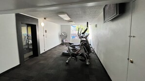 A gym with exercise equipment, a fan, and a door leading to another room. - Studio 6 Suites Tupelo, MS - North (Tupelo)