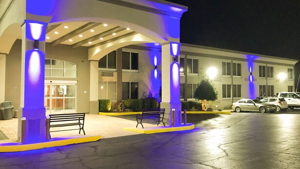 A hotel entrance with a covered waiting area, a bench, and a car parking lot. - Studio 6 Suites Tupelo, MS - North (Tupelo)