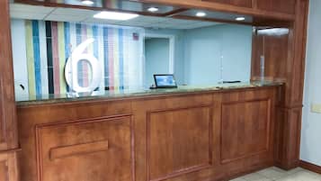 A reception area with a wooden counter, a large mirror, and a small desk with a computer.