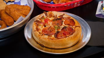 Una pizza con pepperoni y verduras sobre un plato de metal.