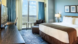 A hotel room with a large bed, a desk with a TV, a view of the outdoors, and a small side table.