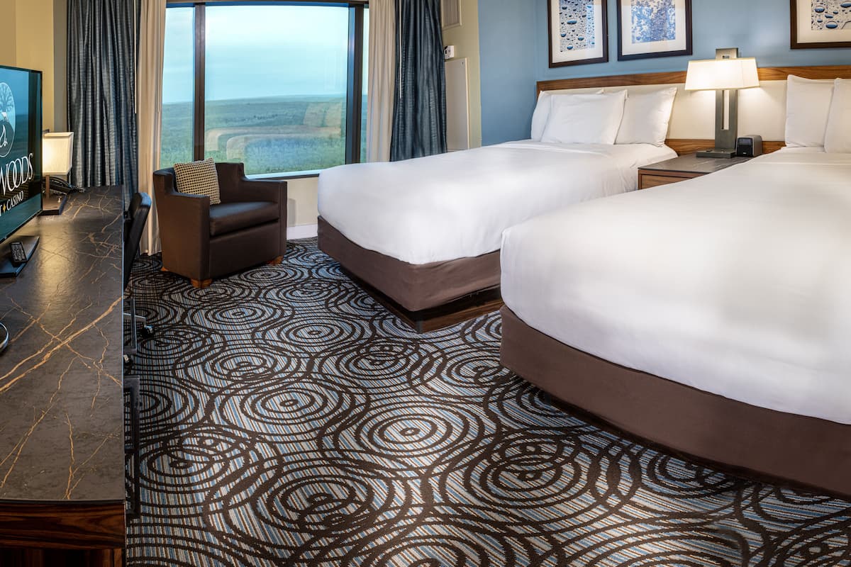 A hotel room with two beds, a desk with a computer, a chair, and a view of the landscape.