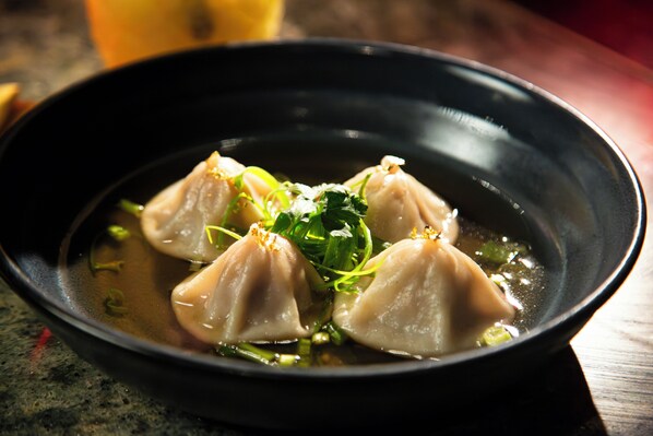 A bowl of dumplings in a clear broth with green garnish.