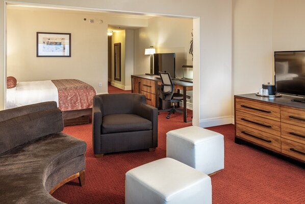 A hotel room with a bed, a sofa, a desk with a computer, a TV, and a dresser.