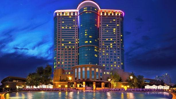 A large hotel with a pool in front, featuring a modern design and multiple floors.