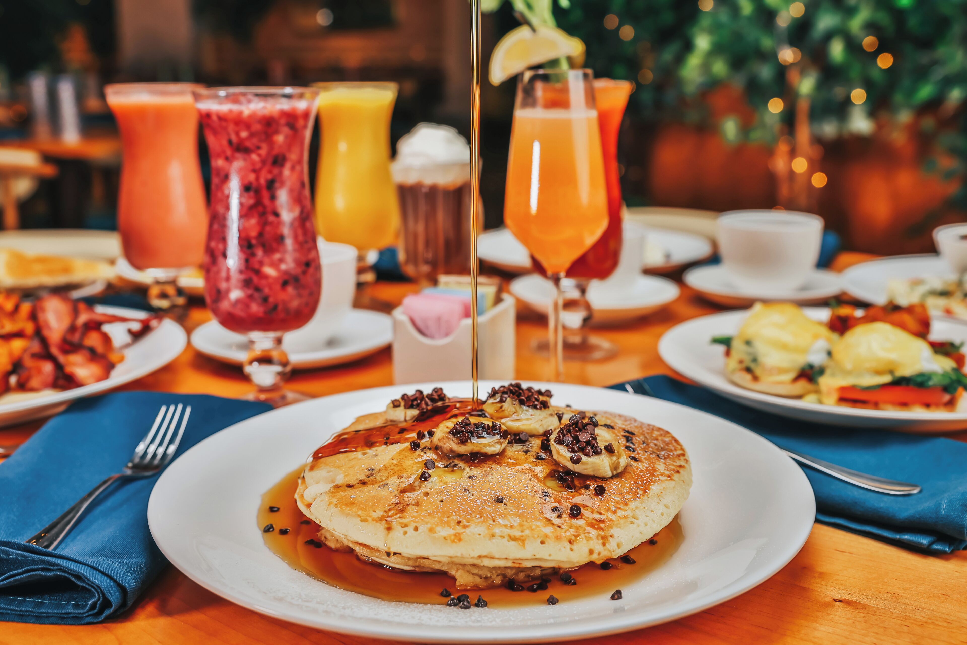 A breakfast setting with pancakes, various drinks, and a variety of side dishes on a wooden table.
