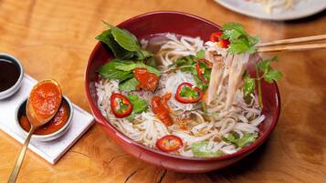 Un tazón de sopa de fideos con diferentes ingredientes, una cuchara con salsa y un par de palillos.