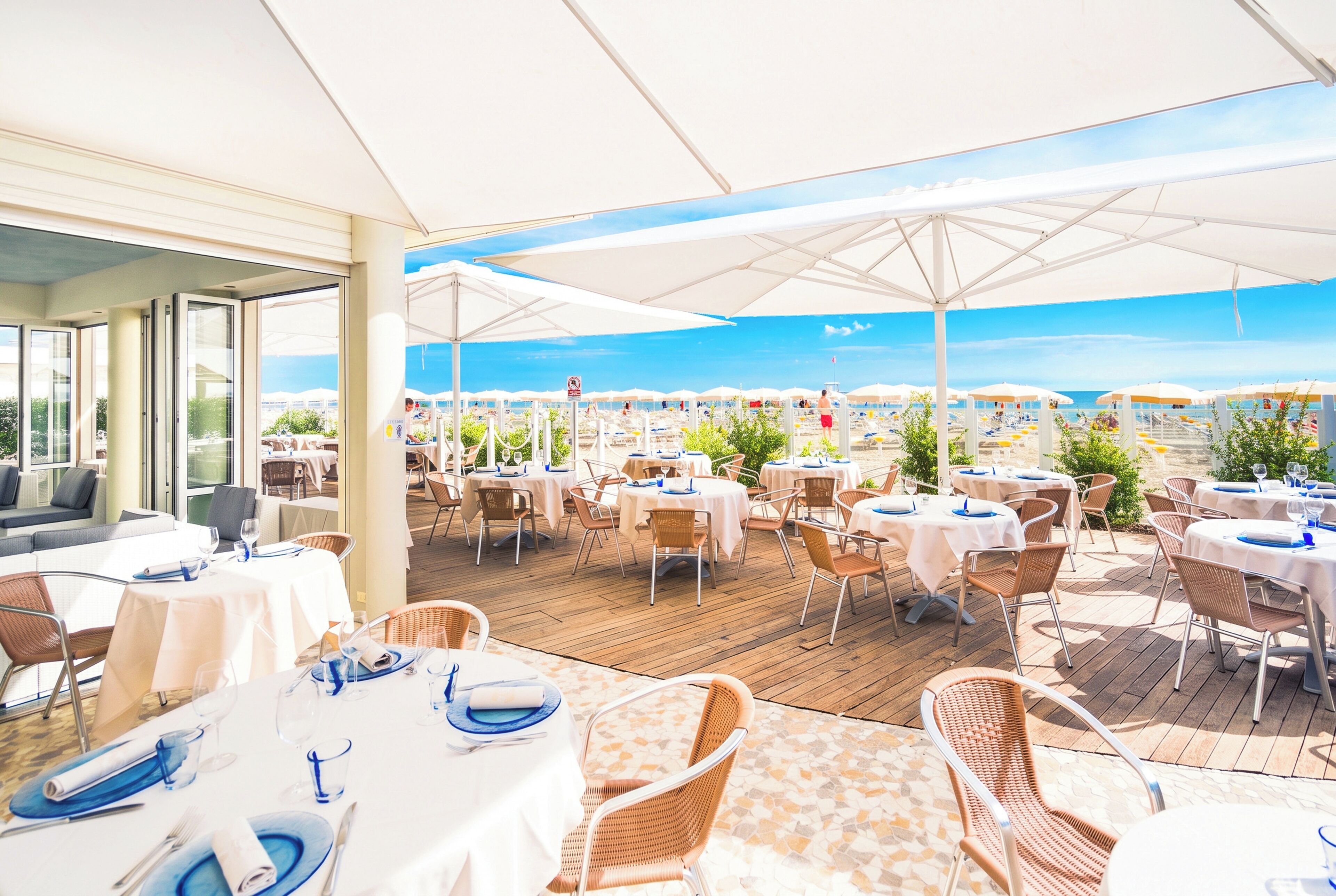 Un área de comedor al aire libre con mesas y sillas, vista al mar y una sección cubierta con sombrillas.