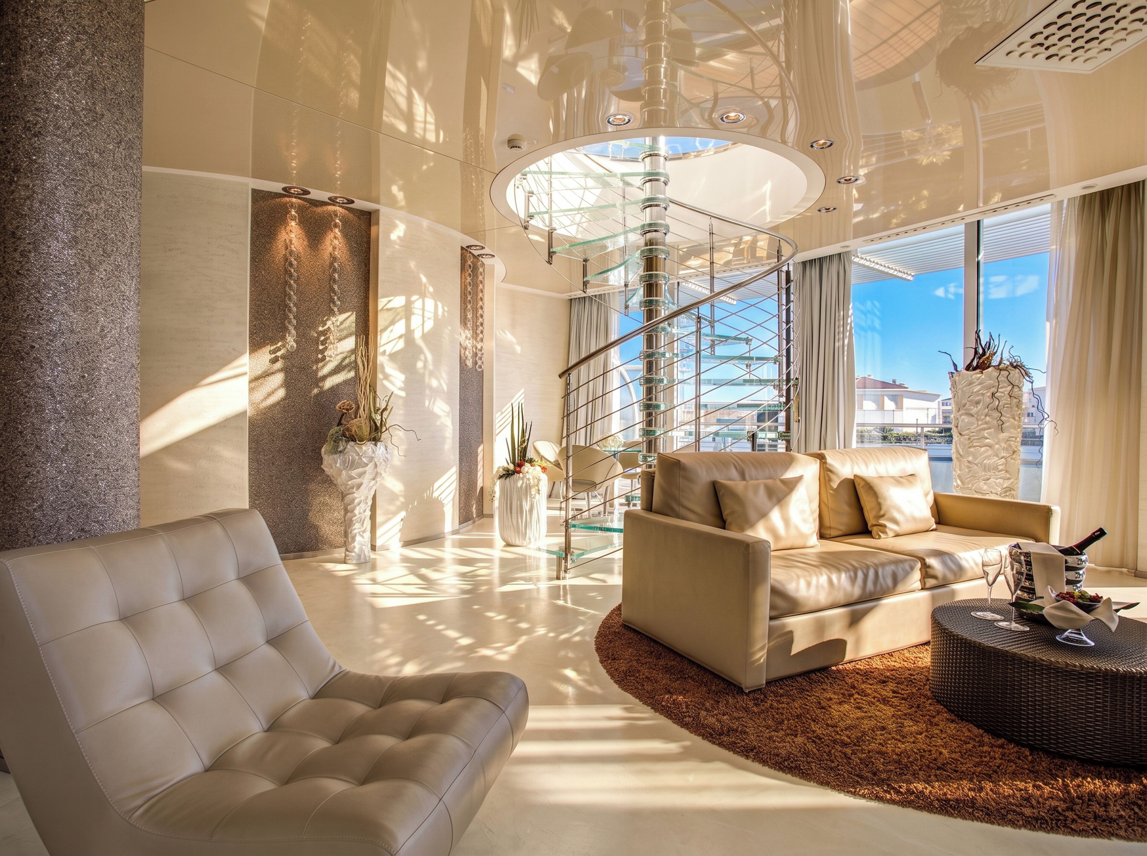 A modern living room with a glass staircase, leather sofas, and large windows.