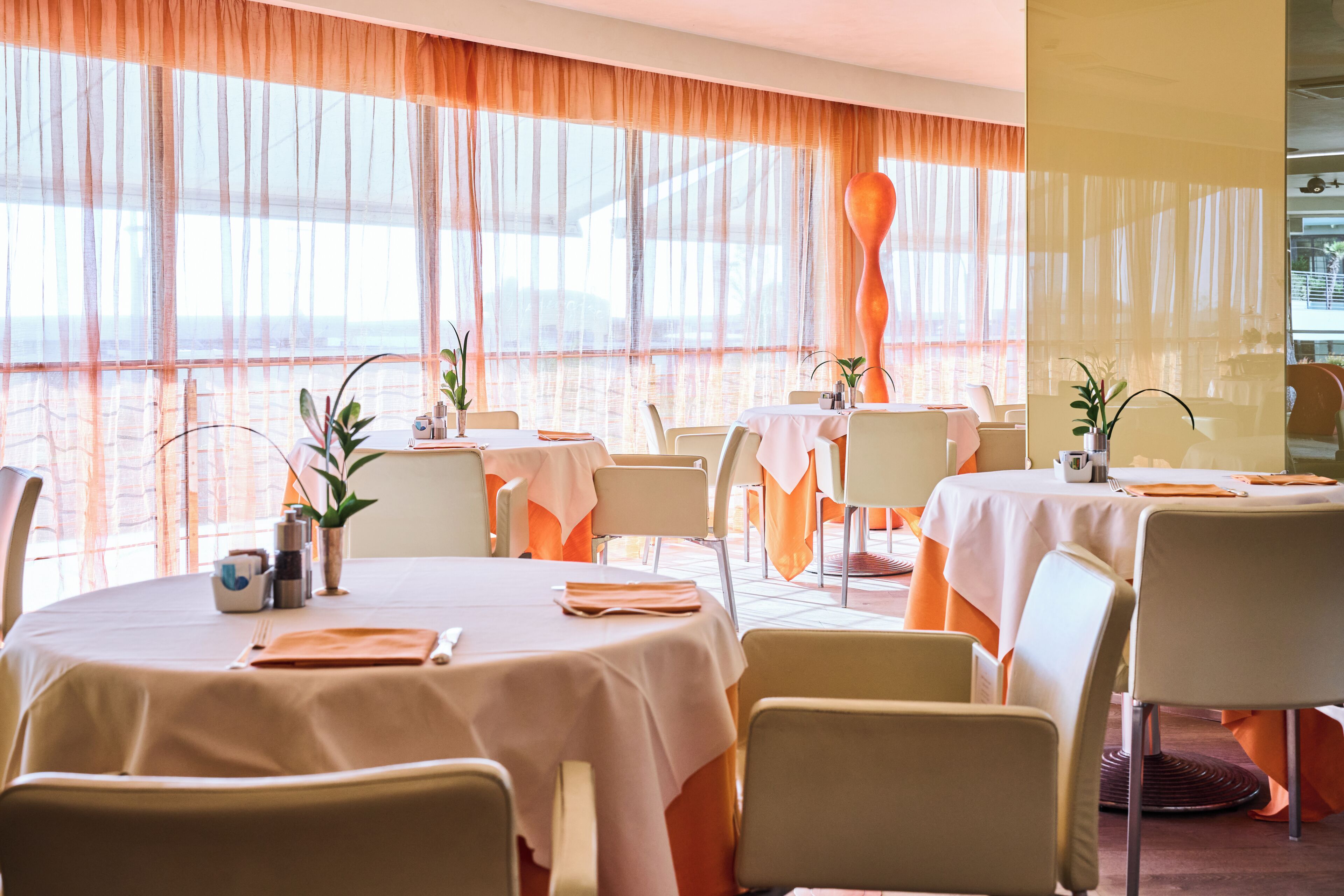 A restaurant with round tables, chairs, and a view of the sea.