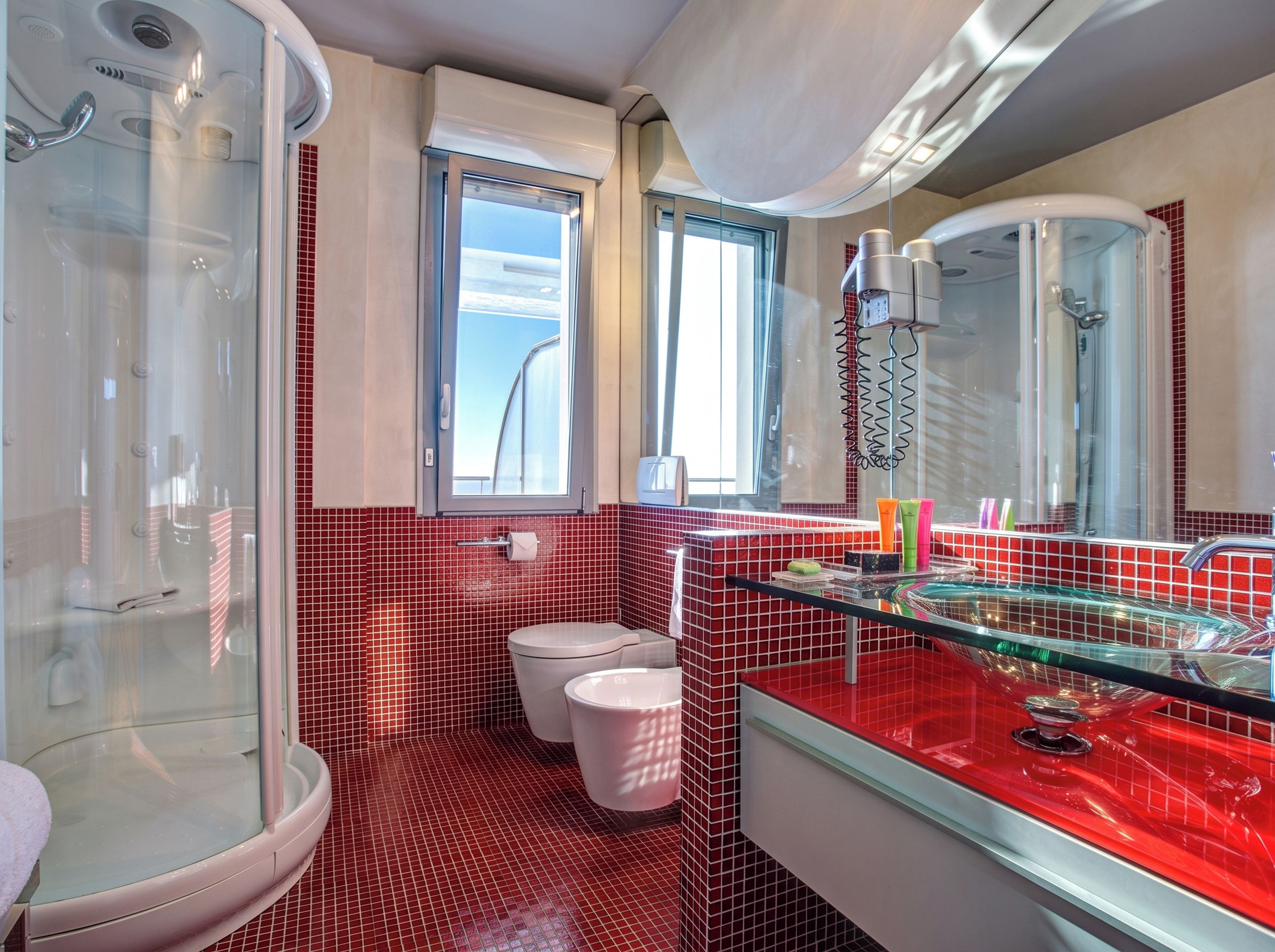 Un baño moderno con ducha envuelta en vidrio, inodoro y tocador con lavamanos de vidrio.