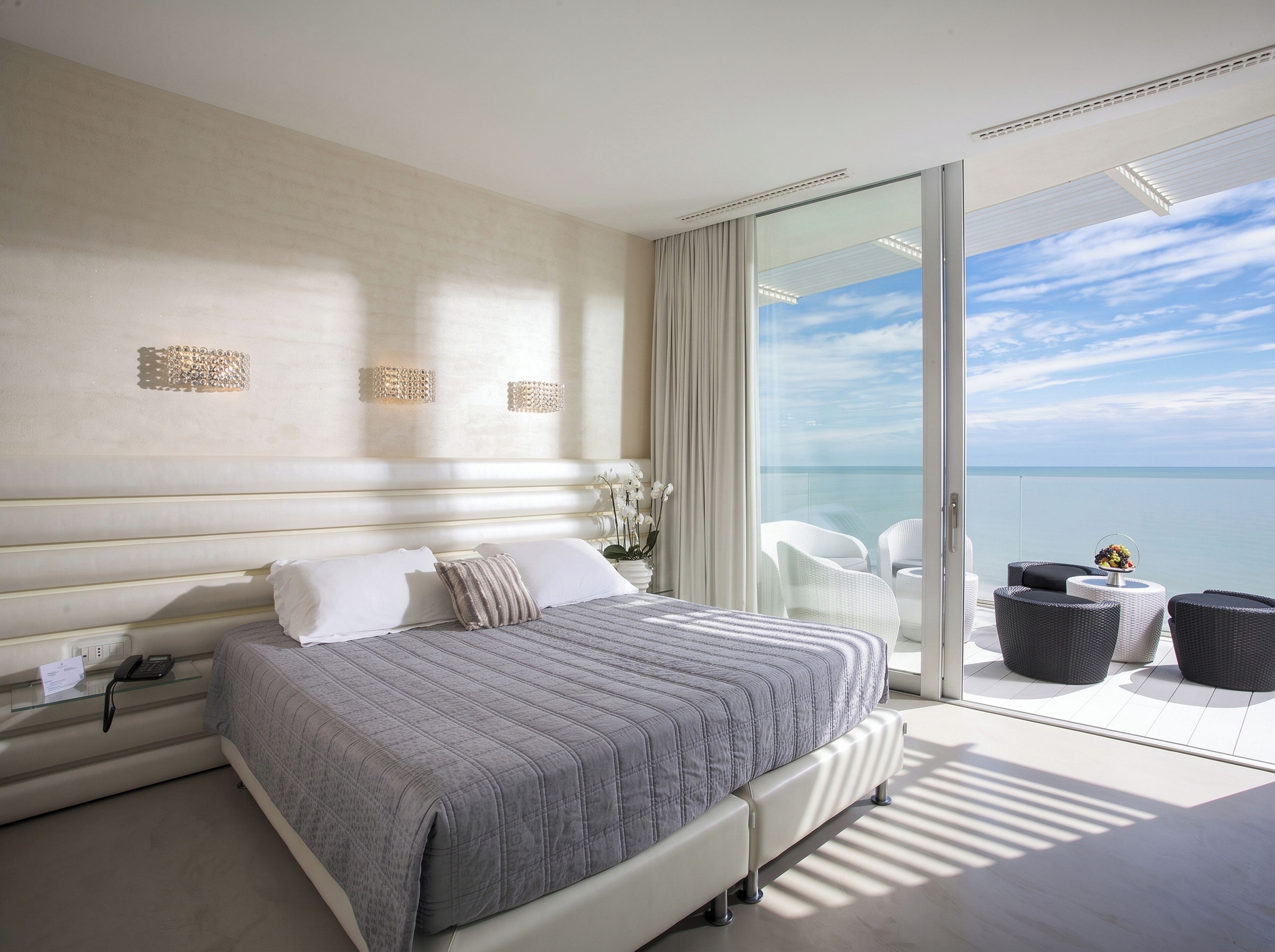 Un dormitorio moderno con una cama grande, una puerta de vidrio que da a un balcón con vistas al mar.