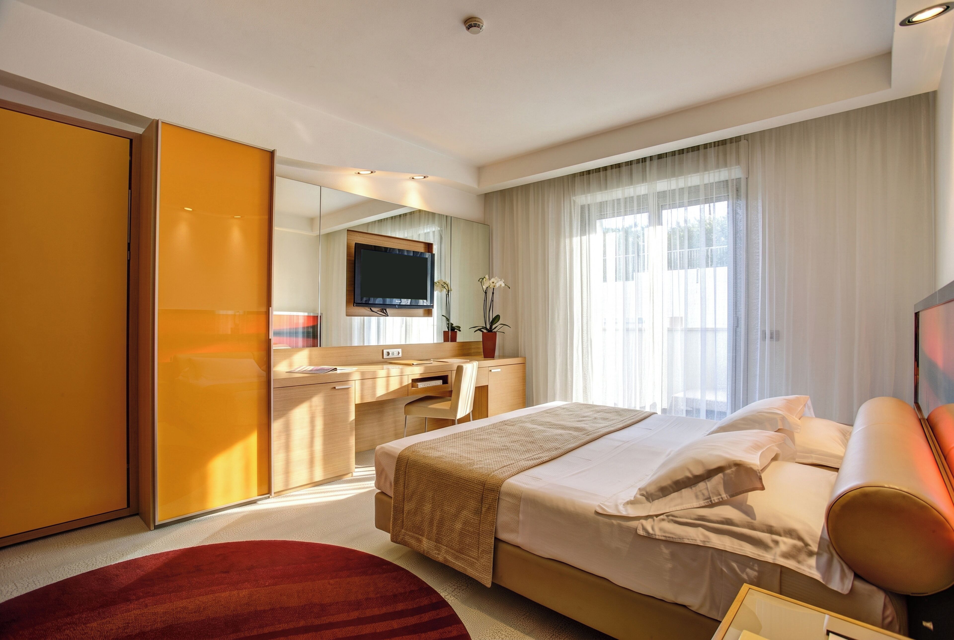 Une chambre d’hôtel avec un lit, un bureau, une télévision et une grande fenêtre avec des rideaux.