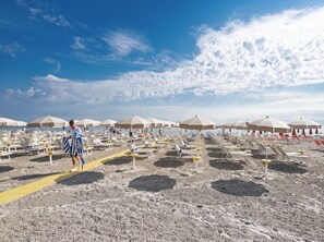 Una playa con filas de tumbonas y sombrillas, un sendero amarillo y un cielo despejado.