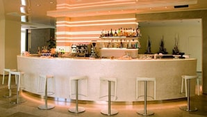 A bar area with a curved counter, multiple stools, and a variety of bottles. - Hotel Carillon (Cervia)
