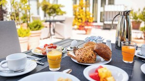 An outdoor breakfast setting with a table set for two, including plates of toast, fruit, and a coffee pot. - Atlantic Hotel Vegesack (Bremen)