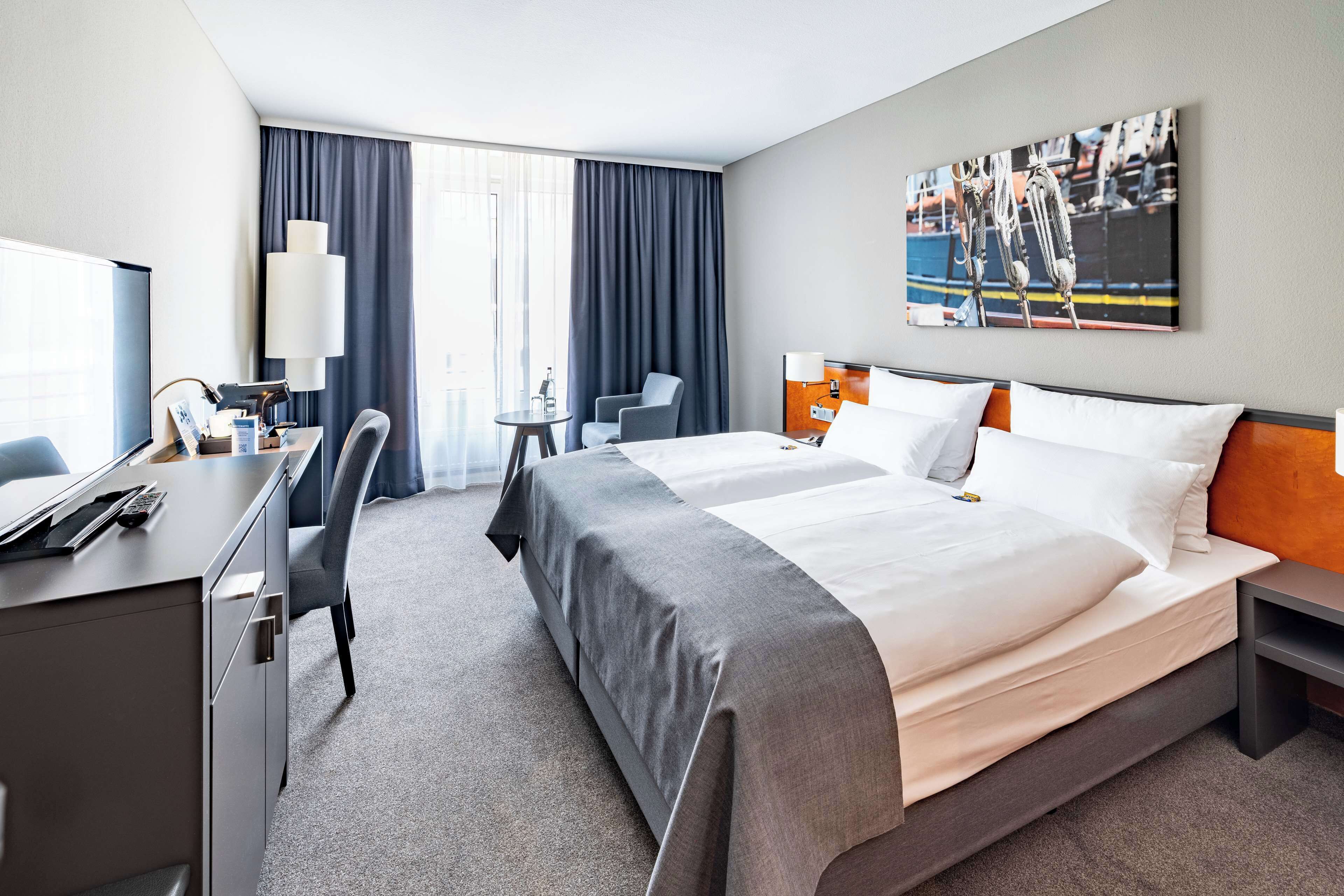 Une chambre d’hôtel avec un grand lit, un bureau avec un ordinateur, une chaise, une petite table et une fenêtre avec des rideaux.