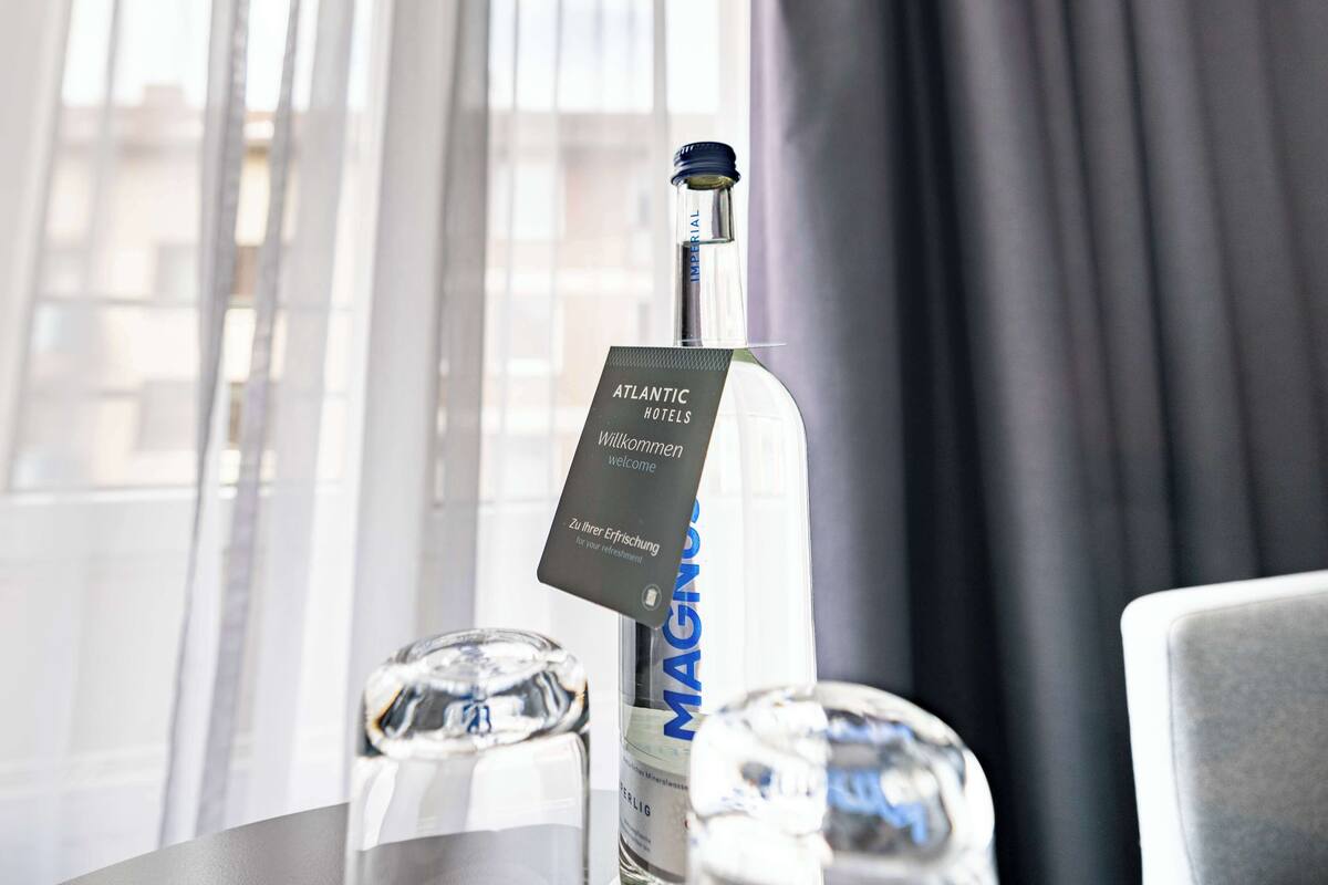 A bottle of MAGNOLIA water with a tag reading "Atlantic Hotels Welcome" and "Zu Ihrer Erfrischung" on a table.