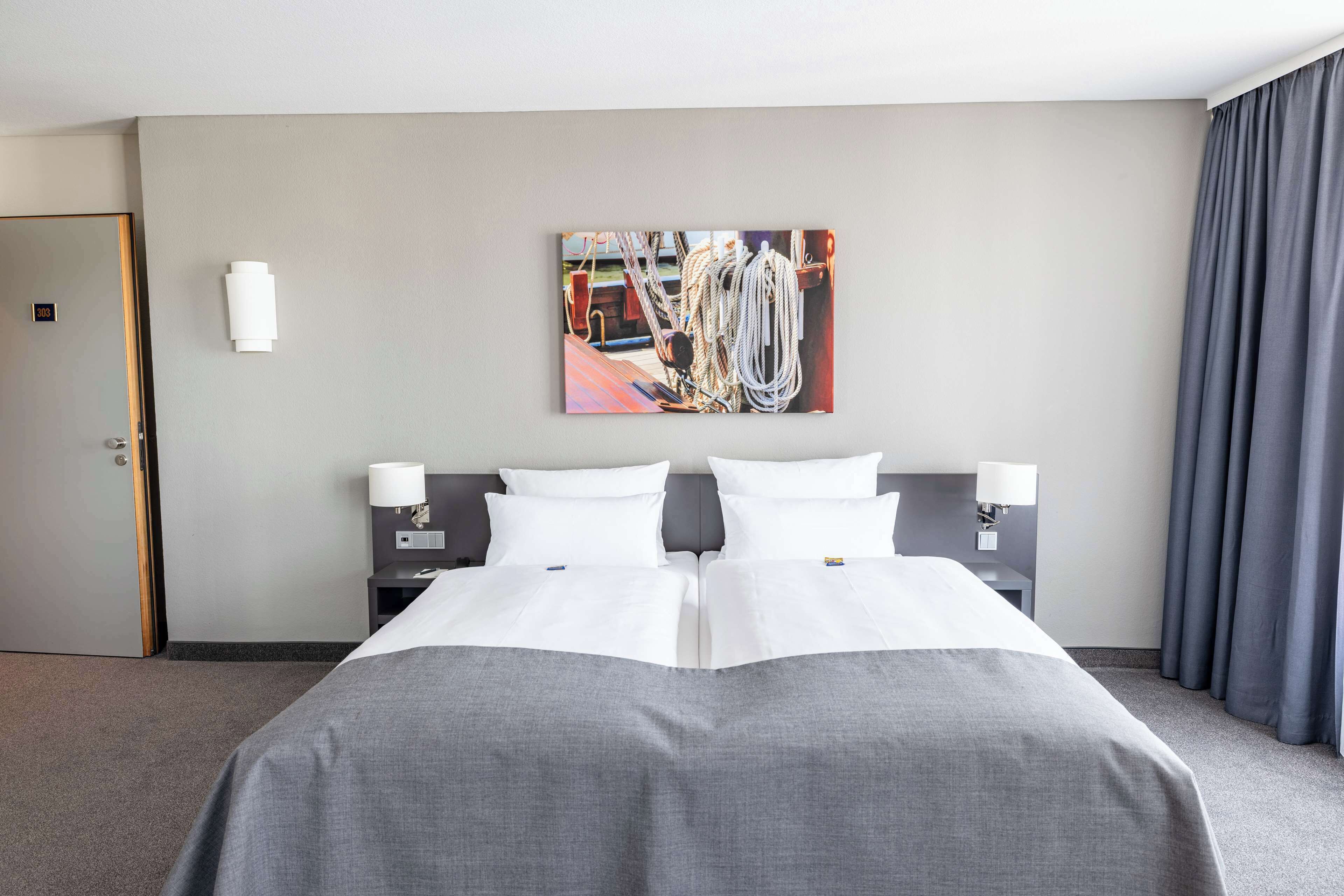 Habitación de hotel con una cama grande, dos mesitas de noche con lámparas, un cuadro en la pared y una puerta.